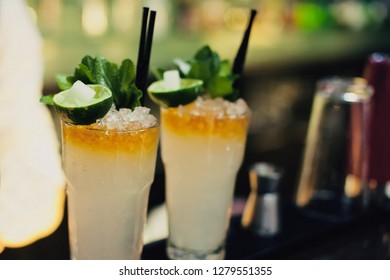 Mojito Classic Cocktails On Bar. Close-up Cold Cocktail With Crushed Ice, Mint And Slice Of Lime With Burning Sugar Cube On Glass At Dark Background. Shaker And Jigger Barmen Equipment.