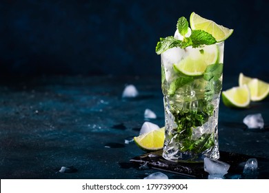 Mojito cocktail or mocktail with lime, mint, and ice in glass on blue background. Summer cold alcoholic non-alcoholic drink,  beverage and cocktail. Copy space