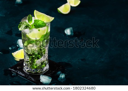 Mojito cocktail or mocktail with lime, mint, and ice in glass on blue background. Summer cold alcoholic non-alcoholic drink,  beverage and cocktail. Copy space