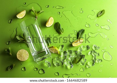 Mojito ingredients on a green background. Lime slices, mint leaves and ice with water drops. Top view.