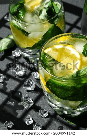 Mojito refreshing cocktail, alcohol drink. Lemonade with lemon and mint leaves on dark background. Trendy shadows Ice cubes. Summer refreshing detox drinks. Clean eating, healthy lifestyle concept, 