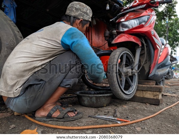 Mojokerto,\
East Java, Indonesia.November,24,2021 a tire patch repairman or\
tukang tambal ban is repairing a leaky motorcycle tire or gembos,\
bocor because it got punctured or tertusuk\
sek