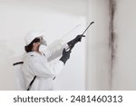 Mold remediation service: A professional worker spraying products to remove mold before house painting, clad in a protective suit and respirator mask, with a backpack sprayer at a home renovation site