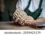 Molding handmade ceramics. Table in pottery studio with female artist shaping wet clay for potter pot or vase. Cropped image of ceramist master or craftswoman shaping kitchenware in creative workplace