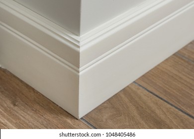 Molding in the interior, baseboard corner. Light matte wall with tiles immitating hardwood flooring