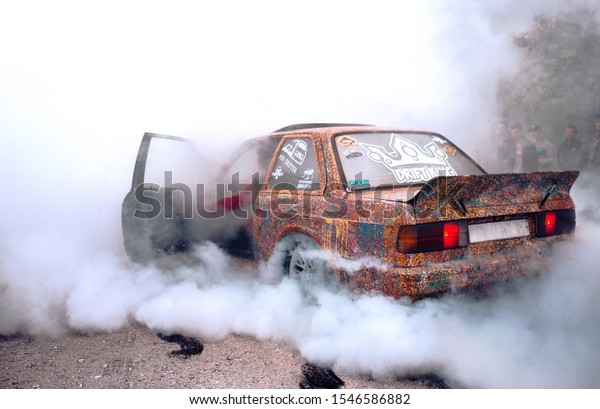 Moldova 25.09.2019.\
Sport modern Car racing car drifting with smoke drift burnout, big\
colourful green blue clouds with wheels and burning tires . Extreme\
street stunts.  