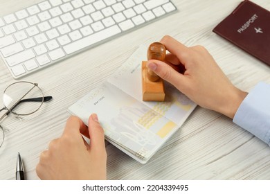 Moldova, Ceadir-Lunga - June 13, 2022: Woman Stamping Visa Page In Passport At White Wooden Table, Closeup