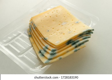 Moldy Spoiled Hard Cheese In An Expired Plastic Transparent Package, Bought At A Supermarket. Photo On A Light Background.