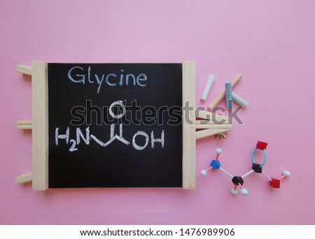 Molecular structure model of glycine molecule with structural chemical formula on a black chalkboard. Glycine (Gly or G) is a proteinogenic amino acid. Black=C, red=O, blue=N, white=H.