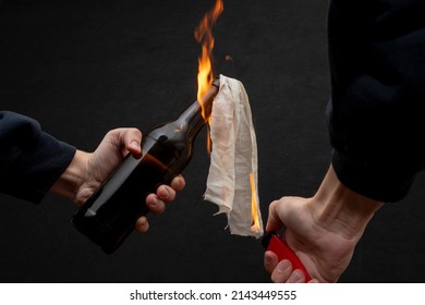 Molotov cocktail is ignited with a lighter on a dark background, close-up, selective focus. Concept: street riots, revolutionary movement, defense and defense, war in Ukraine. - Shutterstock ID 2143449555