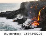 Molten lava flowing into the Pacific Ocean on Big Island of Hawaii, as ocean waves splash onto the rocks and flowing lava