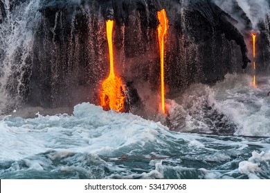 Molten Lava Flowing Into The Pacific Ocean On Big Island Of Hawaii At Sunrise, With Water And Lava Flowing Down Lava Rock Wall As Waves Crash As Seen From A Tour Boat