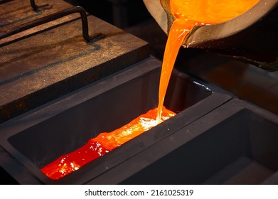 Molten silver is poured from the ladle into a black rectangular graphite mold. - Powered by Shutterstock