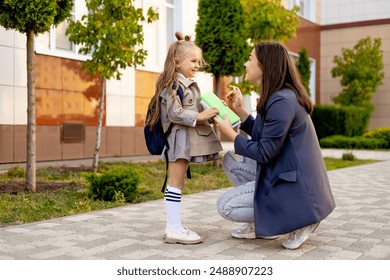 mom accompanies her first-grader daughter to school, kissing her and hugging her, back to school, the parent gives the child to the first grade. Mom meets a student from school. - Powered by Shutterstock