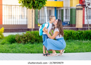 Mom Accompanies Her Son's Child With A Backpack To School Or Kindergarten, Kissing Him, Then Back To School