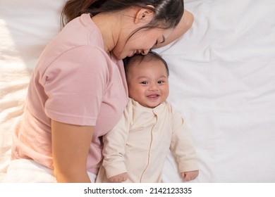 Mom And Baby Are Laying Down And Cuddling. Mom Is Kissing Her Son And Both Are Smiling. Cute Baby Boy Is Look So Happy And Enjoy Playing With Mom On Bed. The Baby Has Chubby And Healthy. Good Moment