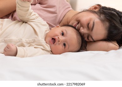 Mom And Baby Are Laying Down And Cuddling. Mom Is Kissing Her Son And Both Are Smiling. Cute Baby Boy Is Look So Happy And Enjoy Playing With Mom On Bed. The Baby Has Chubby And Healthy. Good Moment