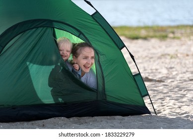 Mom And Baby Peeking Out Of Tourist Tent. Tent On The Sandy Beach. Camping.