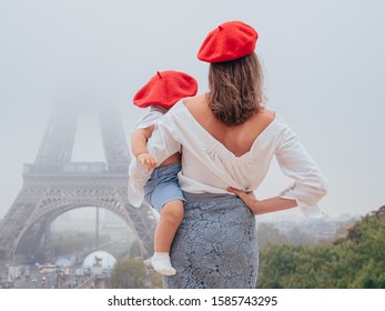 Mom And Baby In Red Berets On The Background Of The Eiffel Tower. The View From The Back