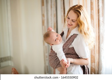 Mom and baby in sling, caring blonde mom gently hugs and plays with her baby son, Sling wear and natural parenthood