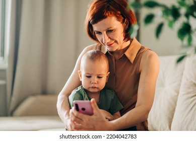 Mom With Baby Watching To Smart Mobile Phone Videos Or Work Text