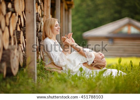 Mom blonde in white dress playing with her daughter on her lap and laughing at sunset in summer