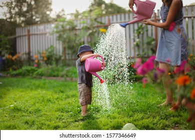 Mom and boy child water the garden together, Mom’s little gardener assistant, taking care of children and garden. Mother watering her son from watering can, take care of trees and plants, wet child - Powered by Shutterstock