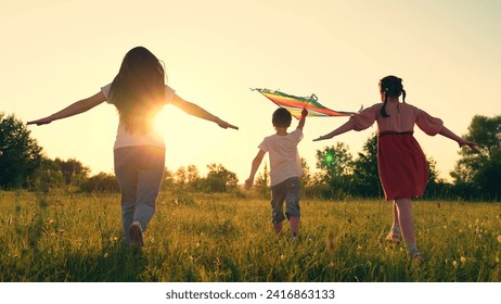 Mom Boy, girl play with toy kite in park in spring. Children toy plane. Kite flies in hands of child in summer in park. Family dreams of traveling, child runs across field at sunset, raising his hands - Powered by Shutterstock