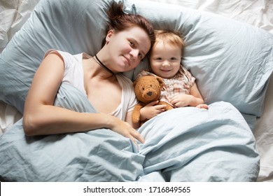 Mom Caucasian Woman In Pajamas With Baby Sleeping On Bed, Top View. Early Morning Mom And Baby, A Cozy Bright Bedroom, Bedding.