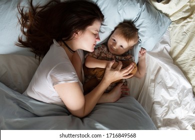 Mom Caucasian Woman In Pajamas With Baby Sleeping On Bed, Top View. Early Morning Mom And Baby, A Cozy Bright Bedroom, Bedding.