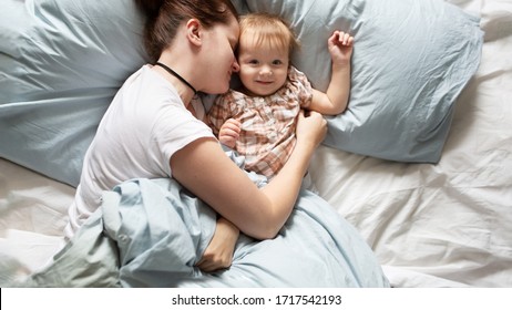 Mom Caucasian Woman In Pajamas With Baby Sleeping On Bed, Top View. Early Morning Mom And Baby, A Cozy Bright Bedroom, Bedding.