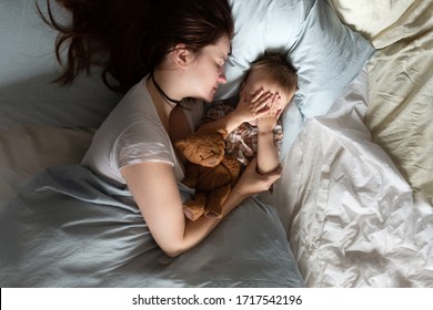 Mom Caucasian Woman In Pajamas With Baby Sleeping On Bed, Top View. Early Morning Mom And Baby, A Cozy Bright Bedroom, Bedding.