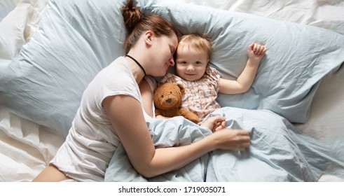 Mom Caucasian Woman In Pajamas With Baby Sleeping On Bed, Top View. Early Morning Mom And Baby, A Cozy Bright Bedroom, Bedding.