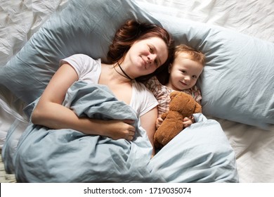 Mom Caucasian Woman In Pajamas With Baby Sleeping On Bed, Top View. Early Morning Mom And Baby, A Cozy Bright Bedroom, Bedding.