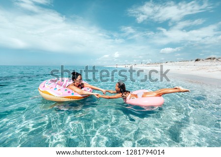 Mom with child chilling on lilo in the sea water. Family relaxing on inflatable rings on the beach. Summer vacations, idyllic scene.