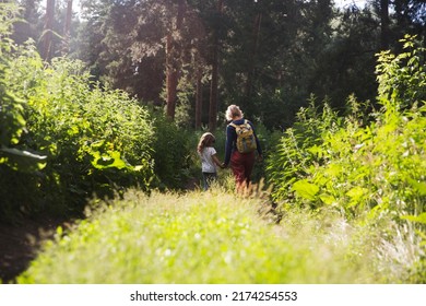mom and and child daughter with backpack walking in the forest. Staycations, hyper-local travel, family outing, getaway, natural environ. Concept of friendly family. Family spends summer time together
