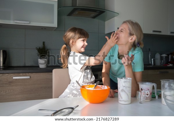 mom and child daughter are cooking pie and having\
fun in the kitchen. casual lifestyle in real life interior. playful\
siblings helping to mother. Concept of friendly family. Family\
spends time togethe