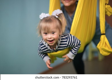 Mom With Child Down Syndrome Engaged In Sport, A Yellow Hammock And A Children's Center,  Concept Childhood, Lifestyle And Toning. World Down Syndrome Day