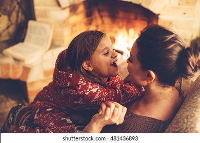 Mom with child playing and chilling by the fire place some cold evening, winter weekends, cozy scene - Powered by Shutterstock