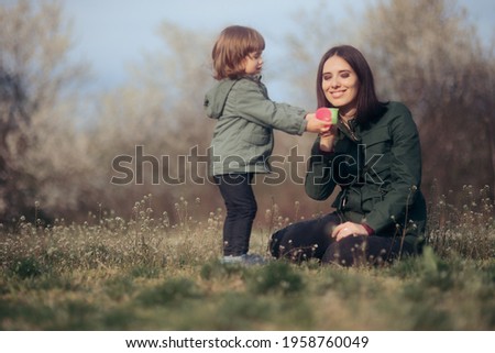 Mom and Child Playing with Teacups Outdoors. Girl pretending to spoon feed her mom reversing roles spending quality time together

