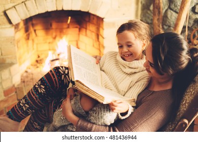 Mom With Child Reading Book And Relaxing By The Fire Place Some Cold Evening, Winter Weekends, Cozy Scene