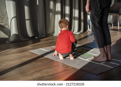 Mom And Child, Toddler, Little Boy Playing Hopscotch, Jumping On Carpet Decorated With Numbers And Squares. Children’s Game Space At Home. Creative Indoors Activities For Kids.