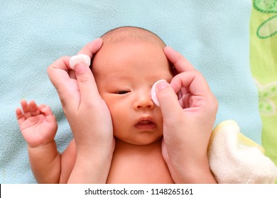 Mom cleaning baby eyes  with care by wet and clean cotton. newborn dirty tears removing.