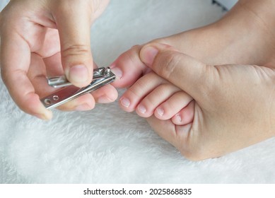 Mom Clipping Her Daughter Toe Nail Against White Background.