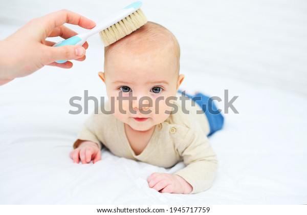 mom combs the baby with a special hair\
brush on a white background. Child\
hygiene.