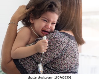 Mom Comforting Baby Toddler Girl. Mixed Race Girl Crying While Holding Spoon.