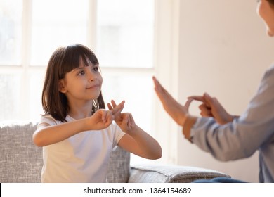 Mom communicating with deaf daughter focus on kid sitting on couch in living room make fingers shape hands talking nonverbal. Hearing loss deaf disability person sign language learning school concept - Shutterstock ID 1364154689