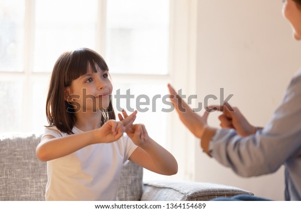 Mom communicating with deaf daughter focus on kid\
sitting on couch in living room make fingers shape hands talking\
nonverbal. Hearing loss deaf disability person sign language\
learning school concept