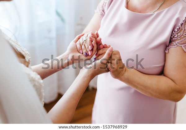 Mom congratulates the bride with\
a marriage and hold hands. woman welcomes. Wedding day holding.\
Concept of relationship between moms and daughters. Close\
up