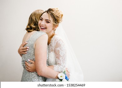 Mom Congratulates The Bride With A Marriage And Hugs. Woman Welcomes. Happy Bride With Mother On Background White Wall In Home. Wedding Ceremony. Close Up